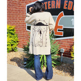 Tan cardigan with black accents of a woman doing a rain dance on the back 